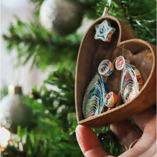 Handmade heart-shaped cinnamon nativity with recycled paper figurines held on a Christmas tree 